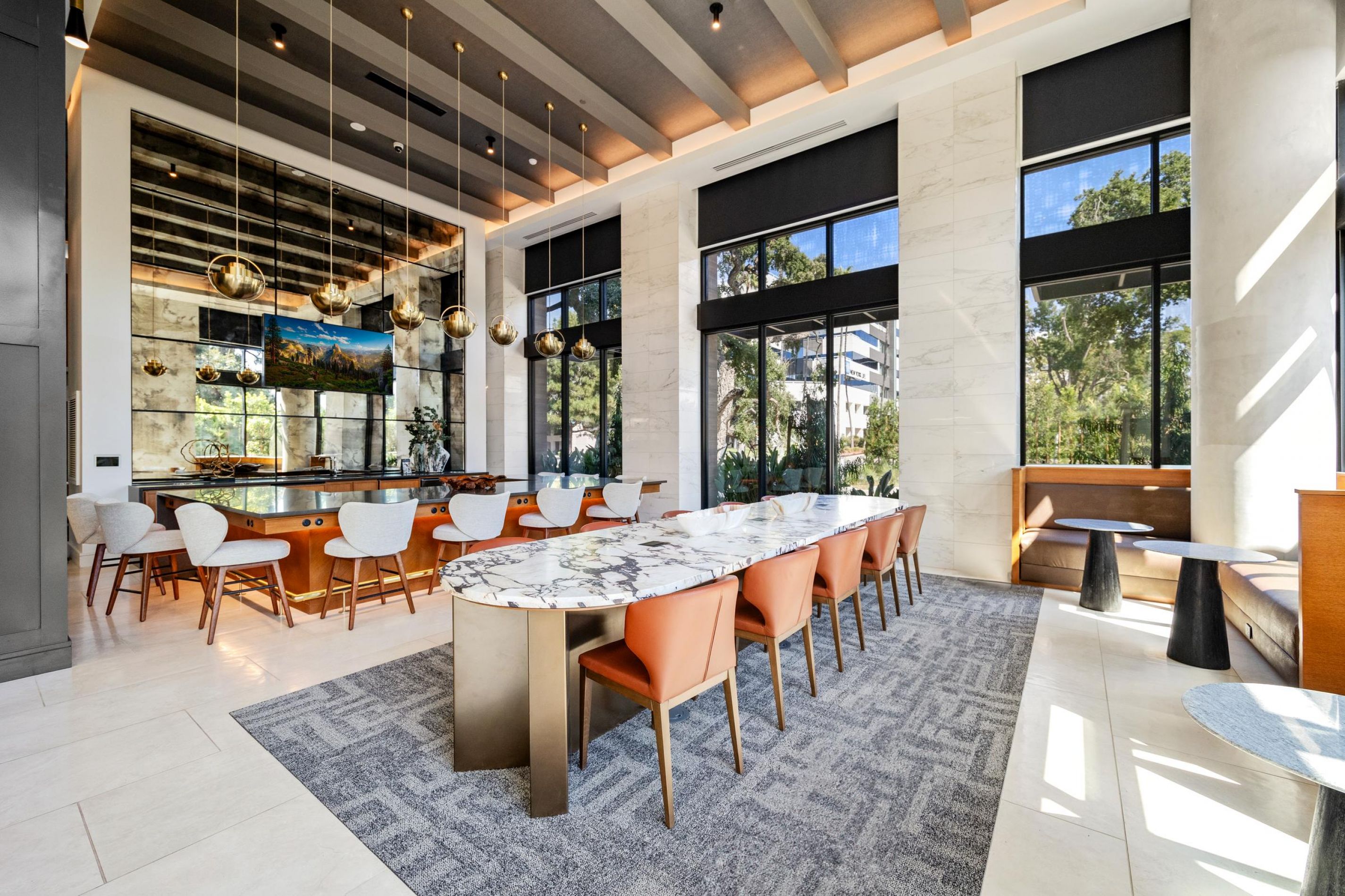 Modern dining area with marble tables, orange chairs, large windows, pendant lights, and gray carpet.