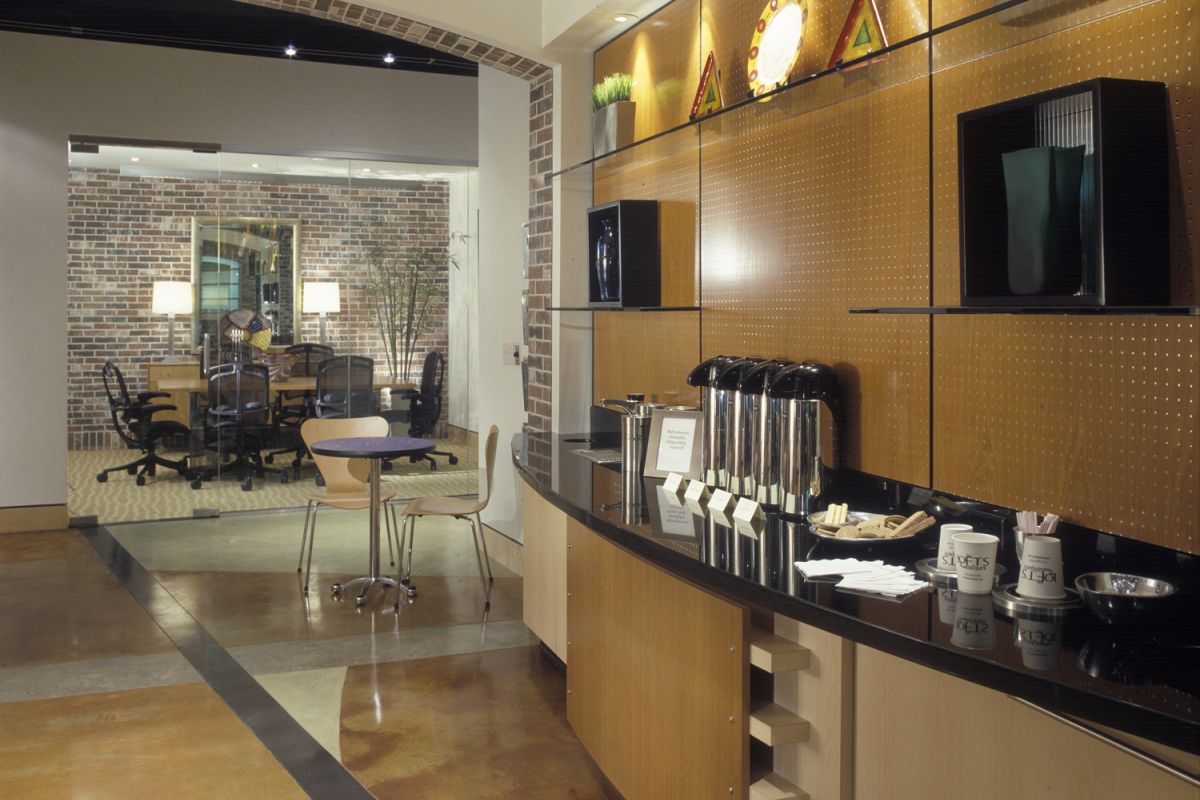 Modern office break area with coffee station in foreground; glass-walled meeting room in background.
