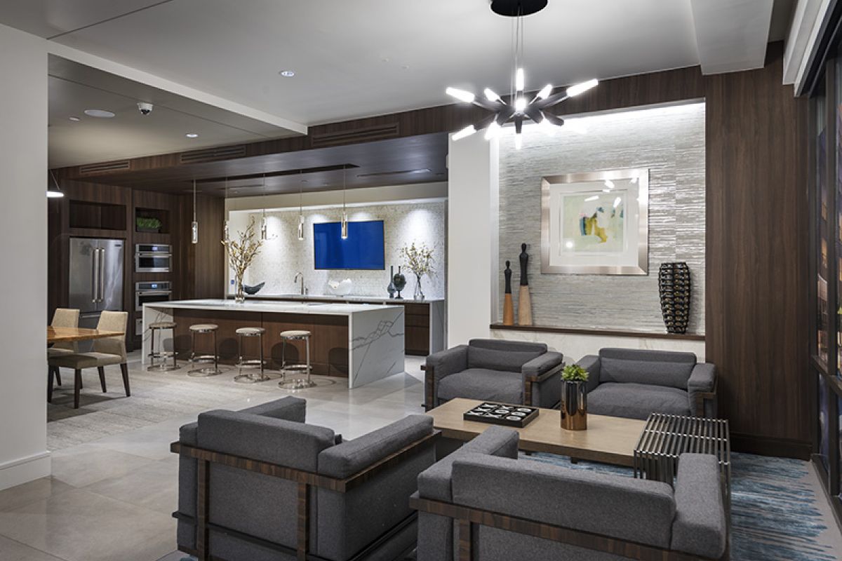 Modern lounge with gray sofas, a kitchen island, dining table, and stylish lighting in a spacious open layout.