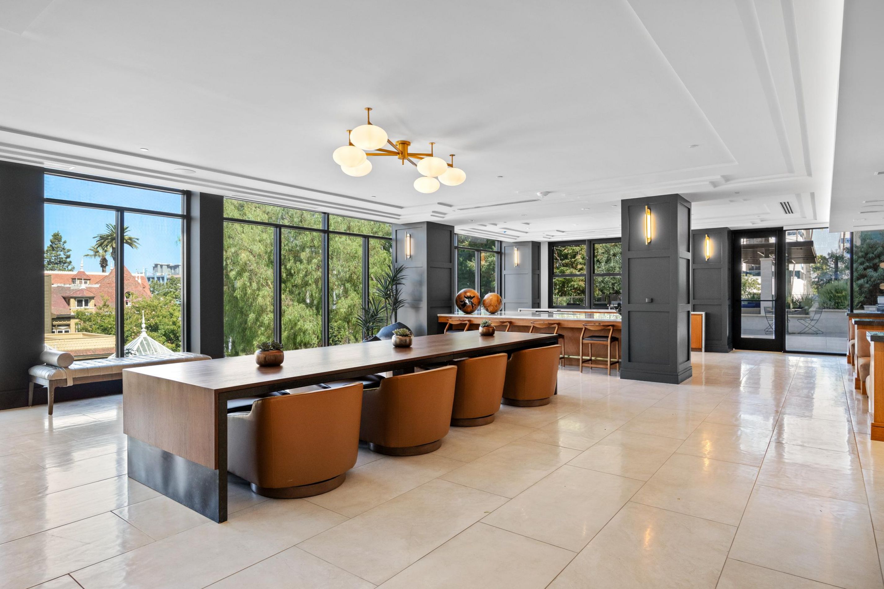 Spacious modern dining area with long wooden tables, brown chairs, and large windows offering a scenic view.
