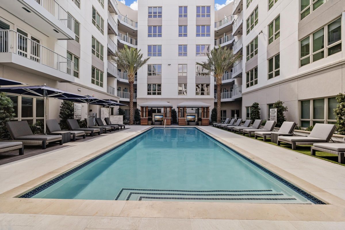 Hanover Laguna Niguel Outdoor pool surrounded by lounge chairs, umbrellas, and palm trees in a modern apartment complex courtyard.