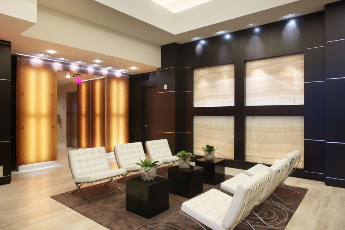 Modern lobby with white chairs, black tables, potted plants, and glowing wall panels in a sleek, stylish setting.