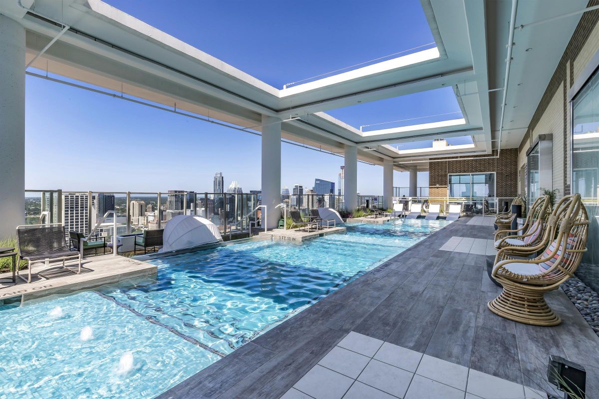 Rooftop pool area with lounge chairs, city skyline view, and modern architecture under a clear blue sky.