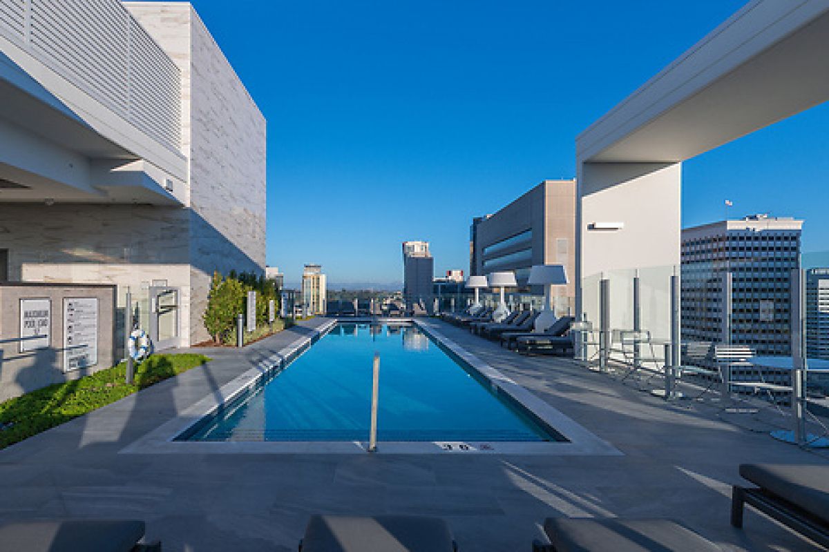 Rooftop swimming pool with lounge chairs, city buildings in the background, and clear blue sky.