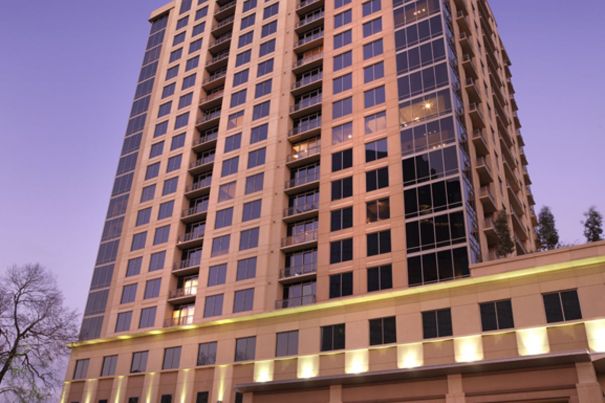Tall modern apartment building with large windows and balconies, lit up at dusk.