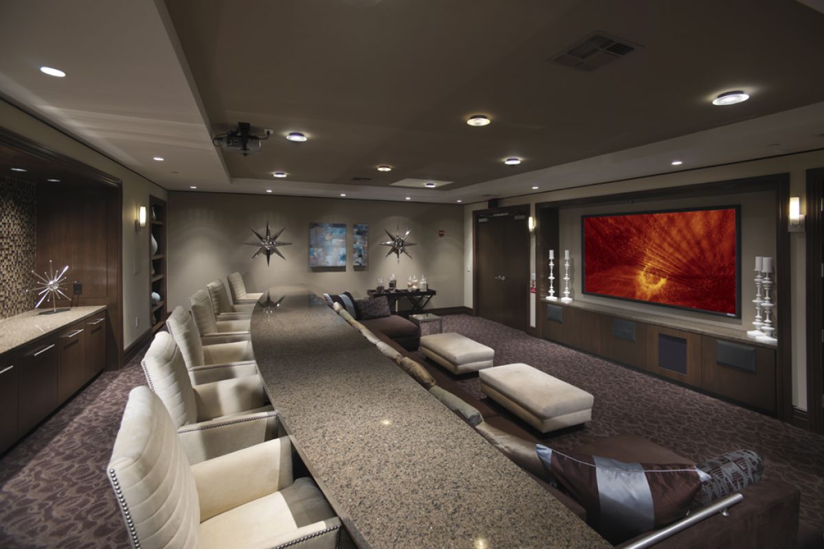 Modern home theater room with a long granite table, plush chairs, large screen, and contemporary decor.