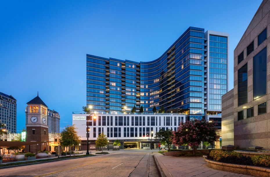 Hanover Company, Hanover Buckhead Village Street view of a modern, curved high-rise building at dusk, with a clock tower and trees nearby.
