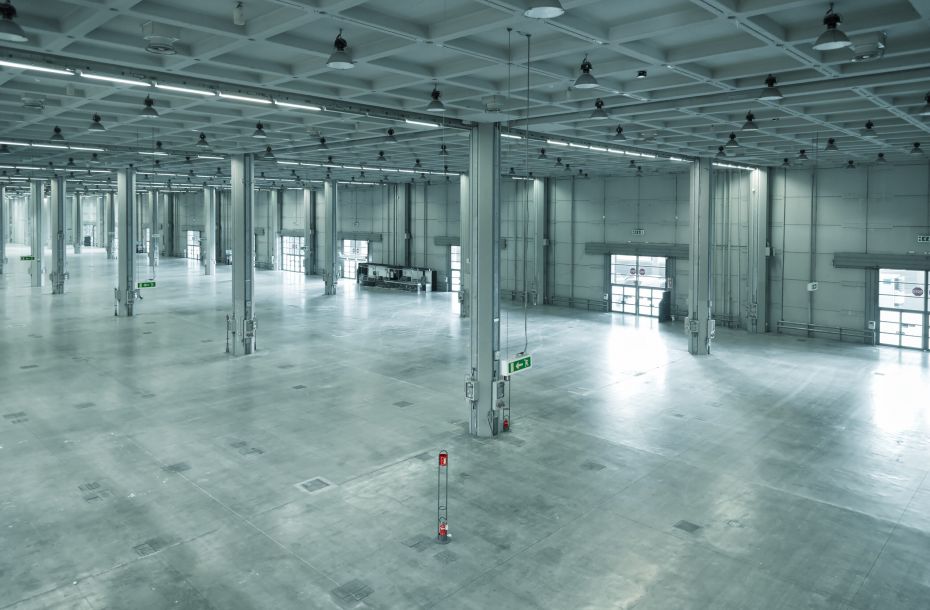 Large, empty industrial warehouse with concrete floors, high ceiling, and support columns.