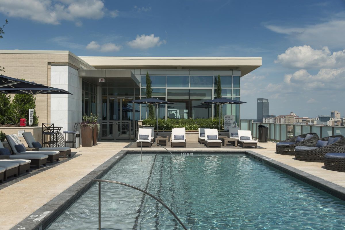 Hanover Company Rooftop pool with lounge chairs and umbrellas, overlooking a cityscape under a blue sky with clouds.