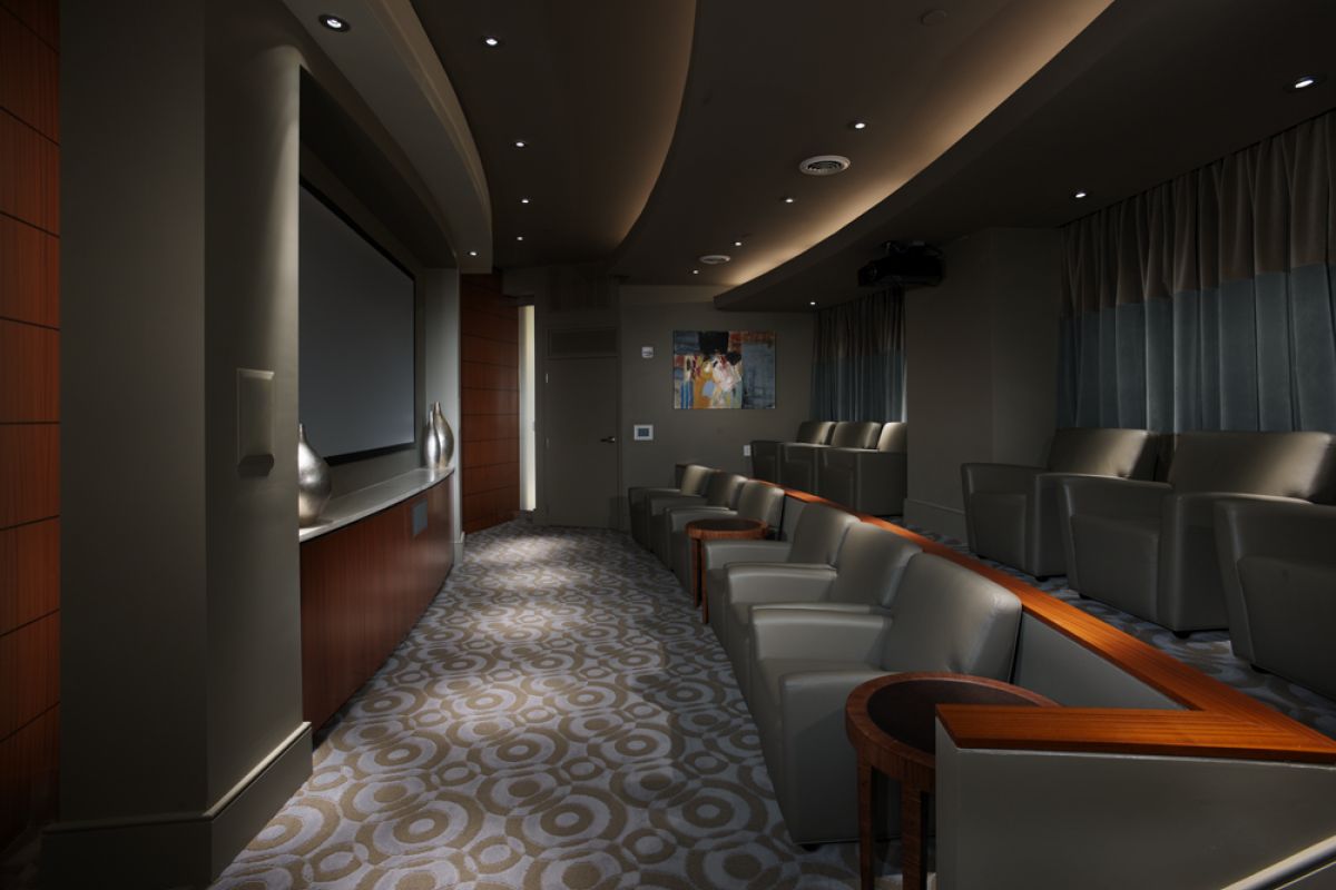 Small, modern home theater with gray seats, patterned carpet, and a large screen at the front.