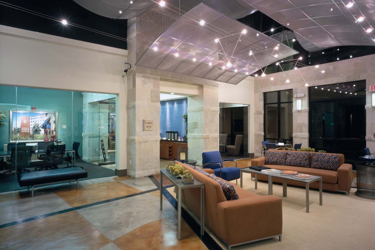 Modern office lobby with brown sofas, glass coffee tables, and a ceiling with decorative lighting panels.