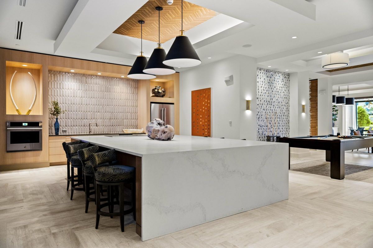 Modern kitchen with large marble island, black pendant lights, barstools, and wood accents. Open space with pool table.