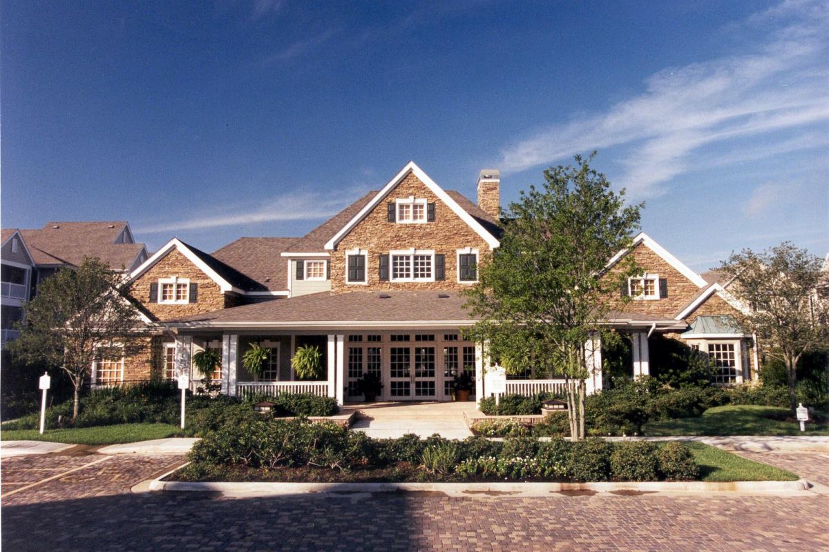 Large two-story Churchill on the Park house with a wraparound porch, gabled roof, and landscaped front yard under a blue sky.