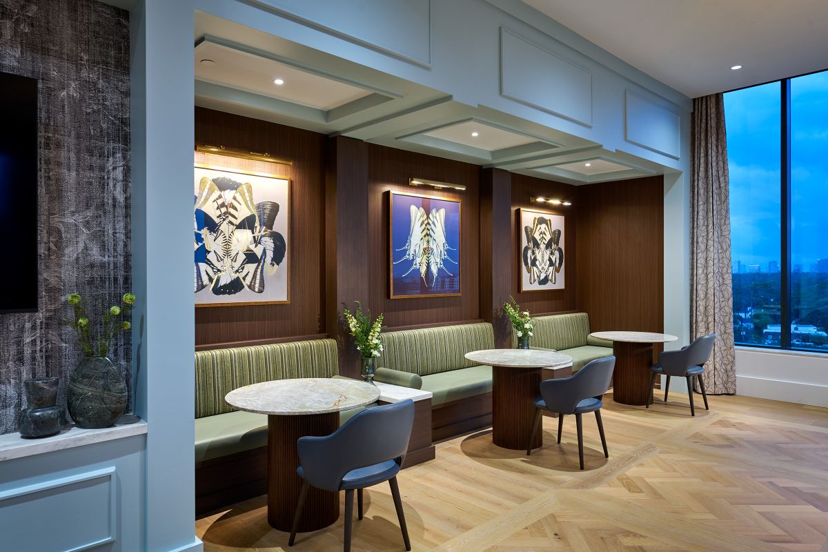 Modern lounge with marble tables, green bench seating, and abstract art at Hanover, overlooking Buffalo Bayou through tall windows.