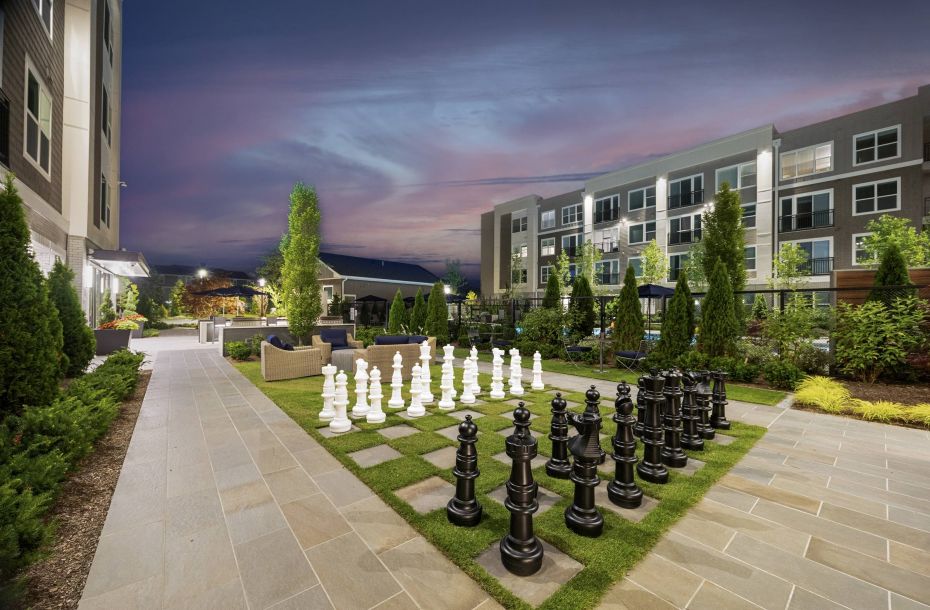 Hanover Company, Hanover at the Pine Hills Outdoor plaza at dusk with a large chessboard, surrounded by modern buildings and greenery.