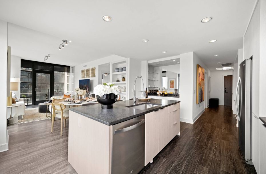 Hanover Company, Hanover Midtown Modern open-plan kitchen with light wood floors, island counter, and living area with large windows in the background.