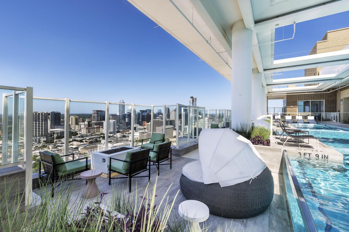 Rooftop pool area with seating, city skyline view, and clear blue sky background.