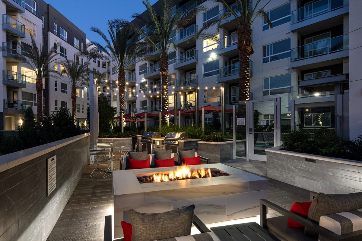 Modern Hanover Diridon courtyard at dusk with fire pit, lounge chairs, palm trees, and string lights—true luxury San Jose apartments.