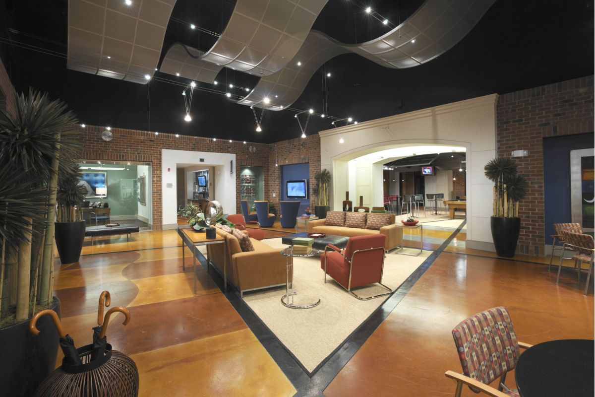 Modern lounge area with brown and red seating, plants, and decorative ceiling panels in a spacious room.