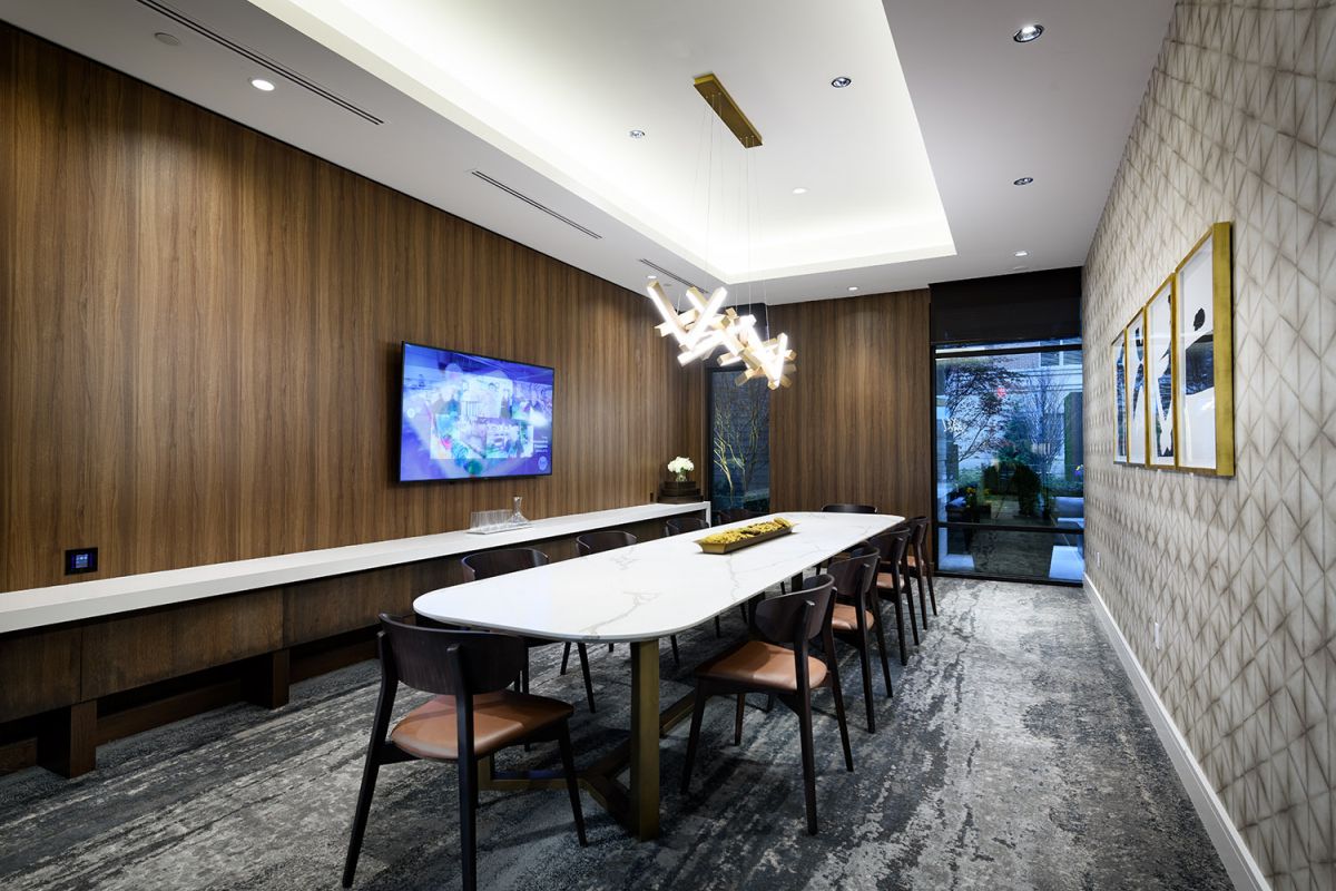 Modern conference room at Hanover with a marble table, wooden walls, TV, and unique chandelier lighting.