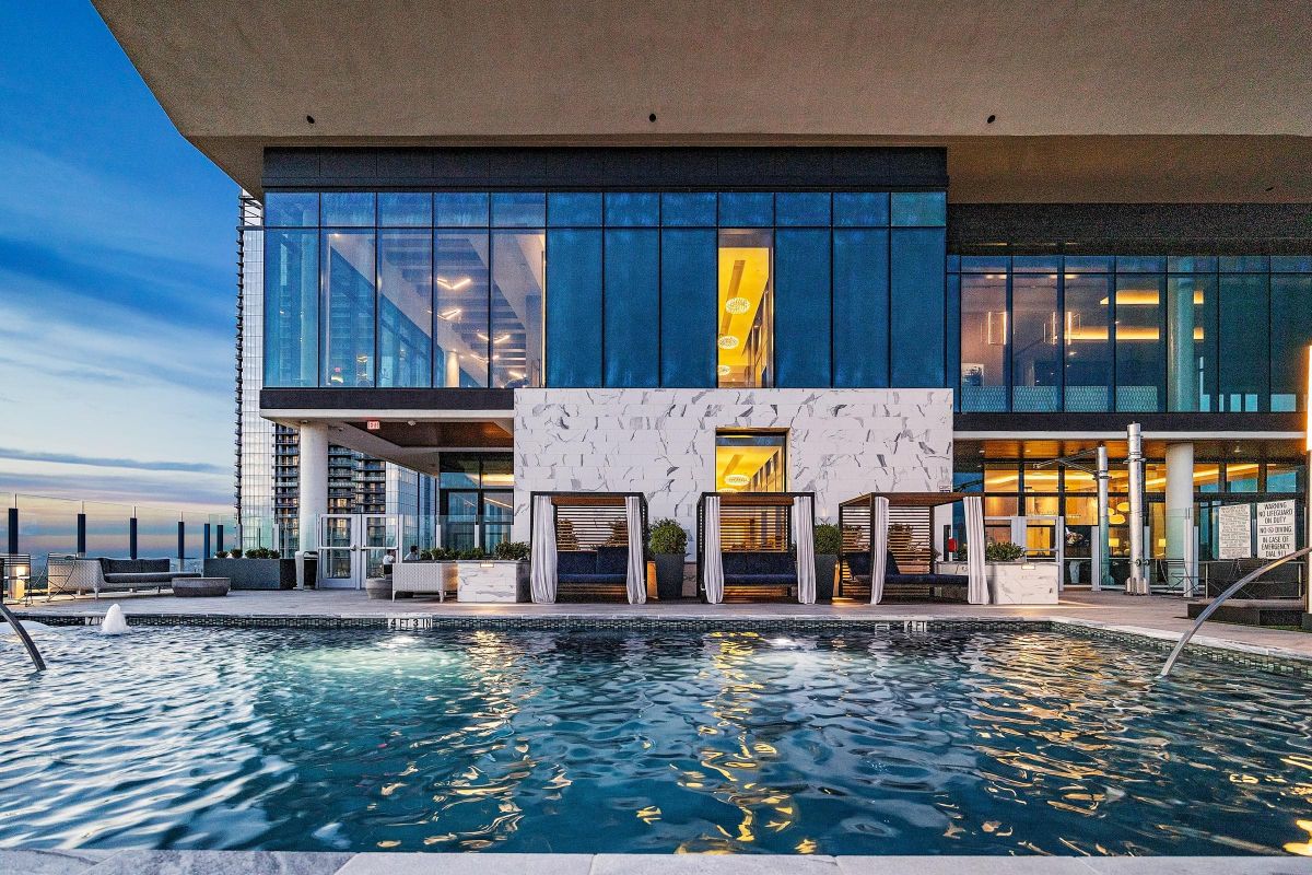 Modern outdoor pool with lounge cabanas and large glass building in the background at sunset.