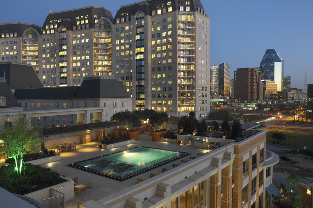 Rooftop pool at dusk with city skyscrapers and lit buildings in the background.