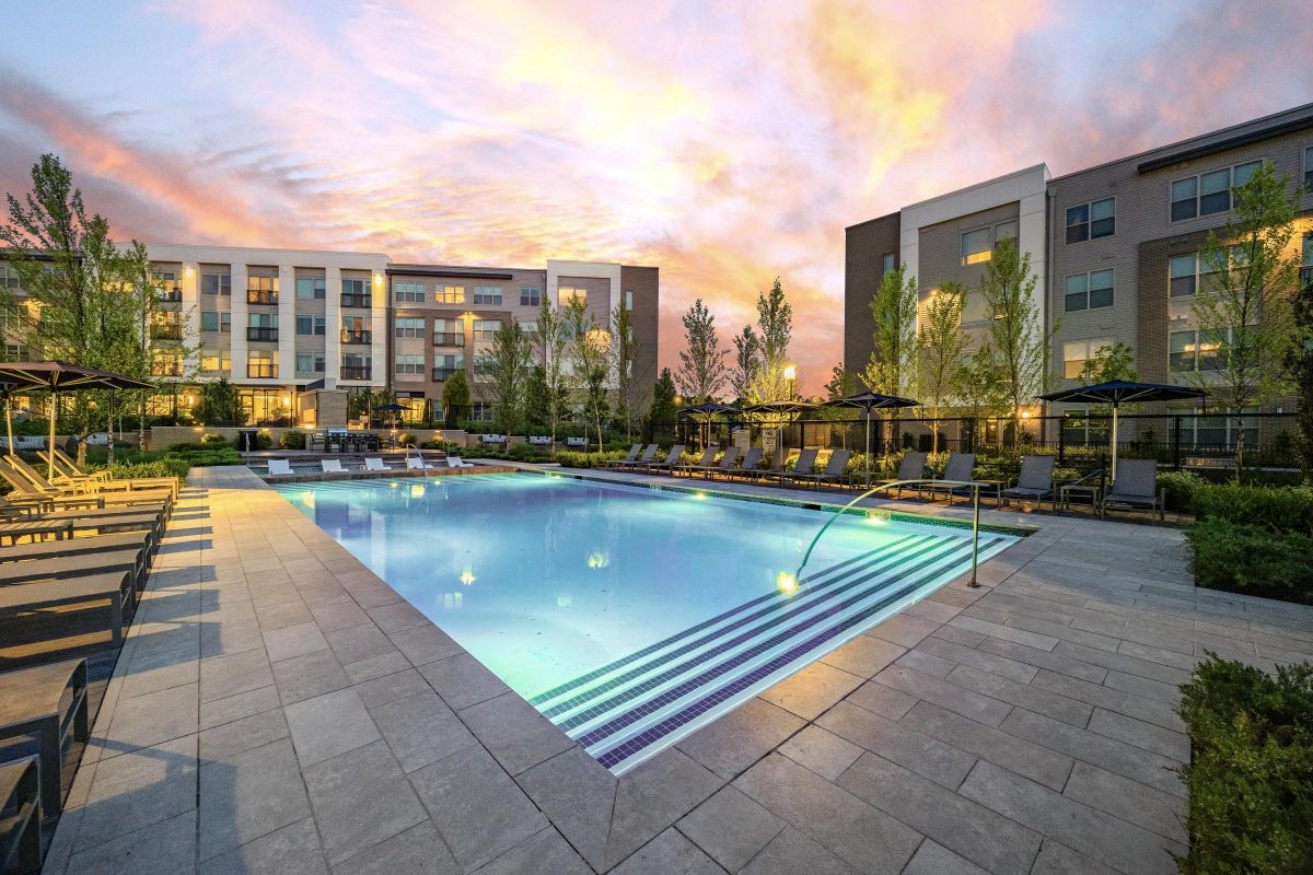 Modern apartment complex at sunset with a large illuminated swimming pool and lounge chairs.