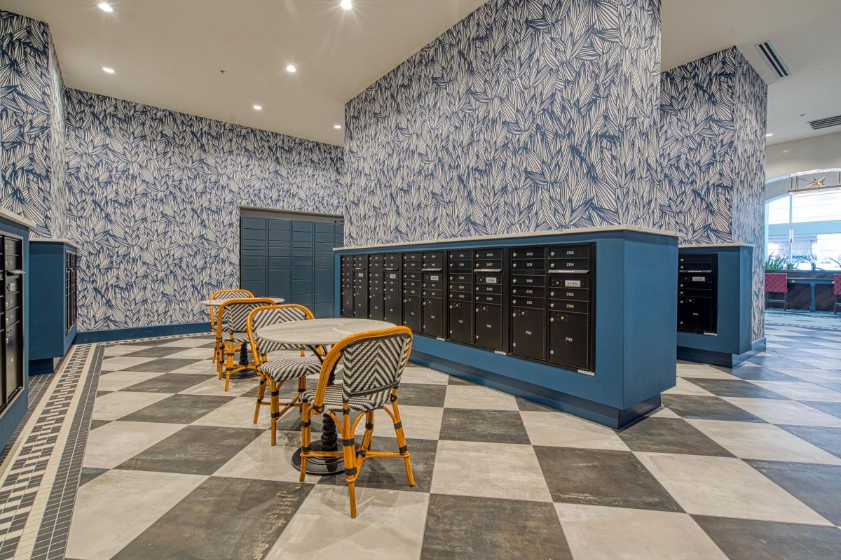 Room with patterned wallpaper, multiple mailboxes, checkered floor, and a small table with wicker chairs.