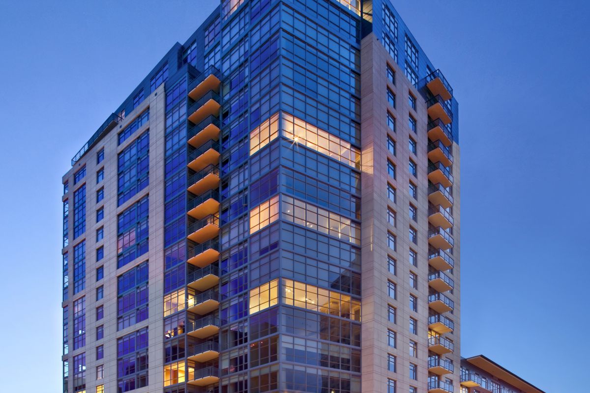 Modern high-rise apartment building with glass windows and balconies, illuminated at dusk.