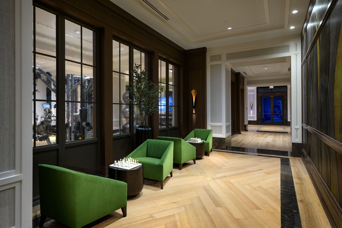 Modern hallway at Hanover with green chairs, chessboards, wood floors, large windows, and warm ambient lighting.