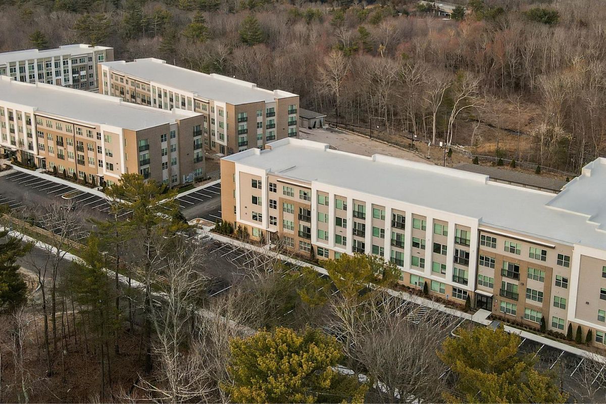 Aerial view of three modern apartment buildings surrounded by trees and empty parking lots.