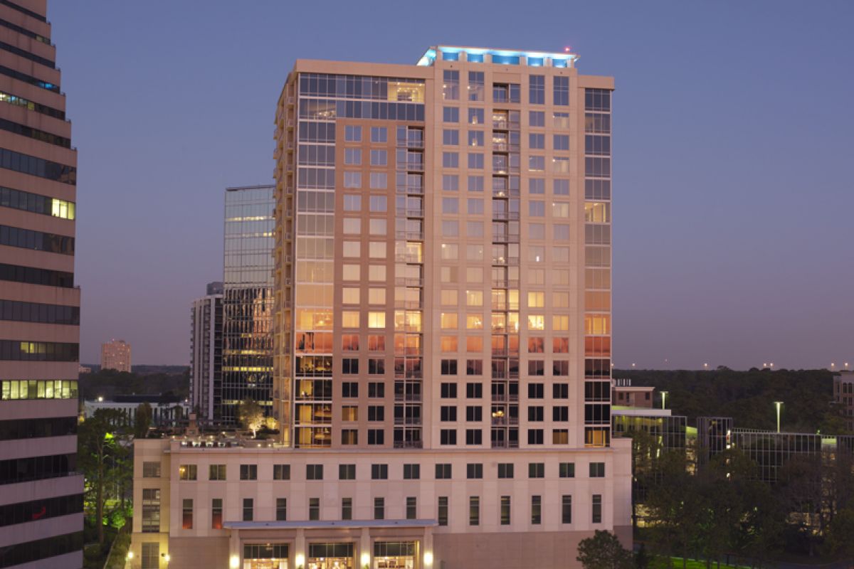 A tall, modern office building at sunset with lights reflecting in its glass windows.