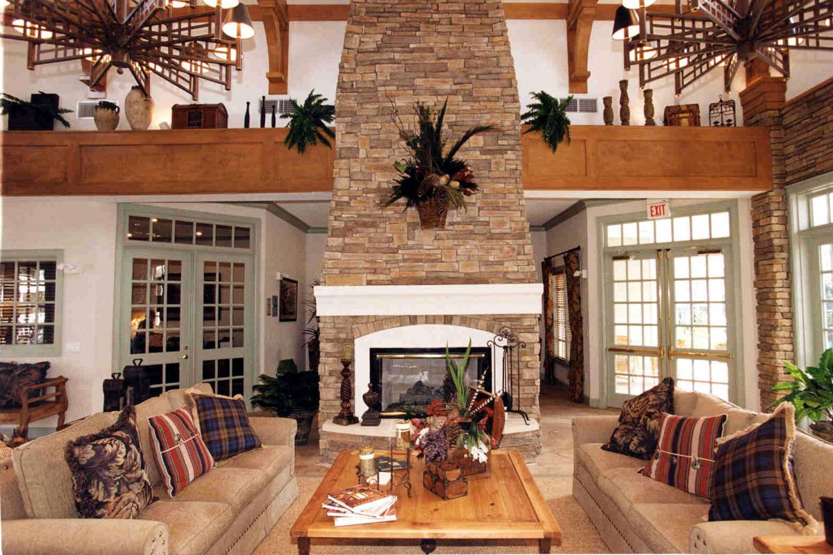 Cozy living room at Churchill on the Park with stone fireplace, sofas, wooden table, lush plants, and patterned pillows.