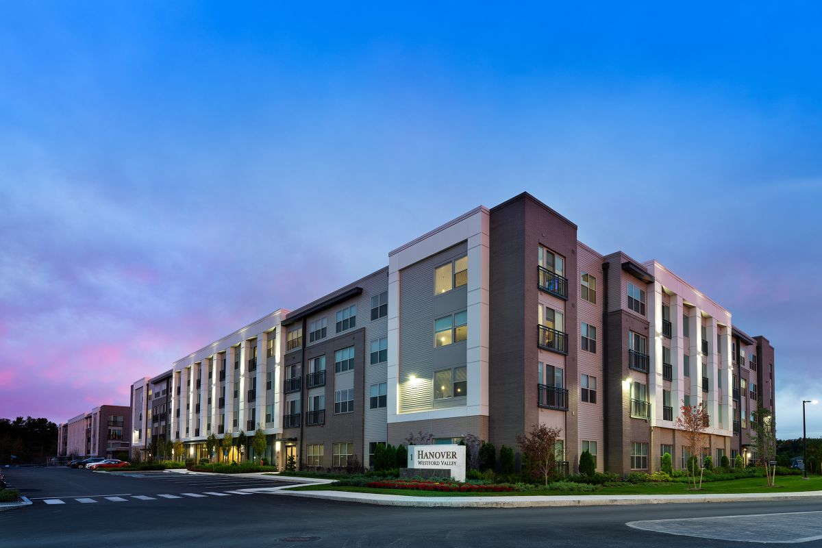 Modern four-story apartment building at sunset with a sign reading "Hanover" in front.