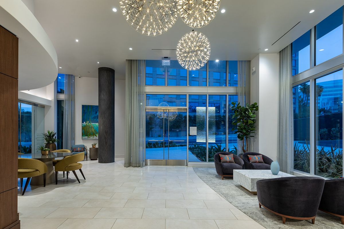 Modern Hanover West LA building lobby with large chandeliers, a stylish seating area, and glass doors leading outside.