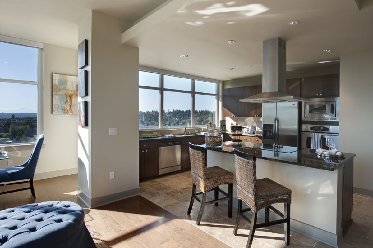 Modern kitchen with bar stools, large windows, and a view of trees and hills in the background.
