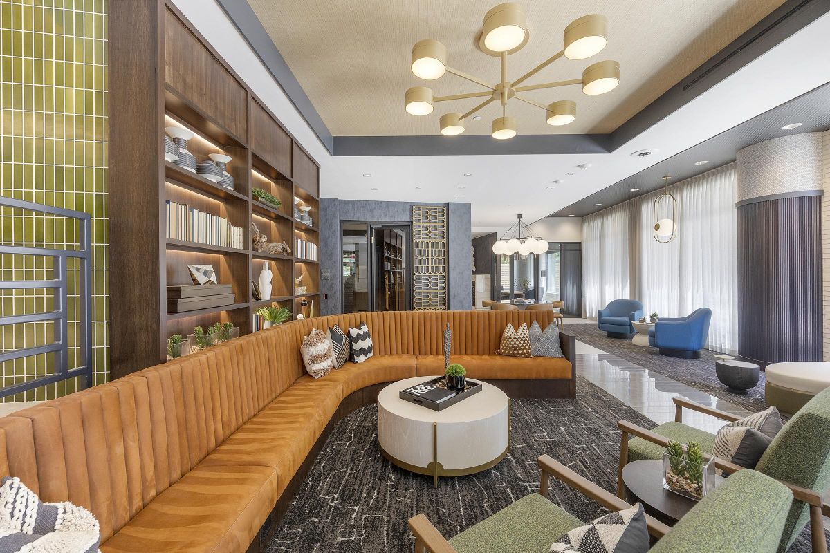 Modern lounge area with a large brown sectional sofa, geometric decor, shelves, and light fixtures.