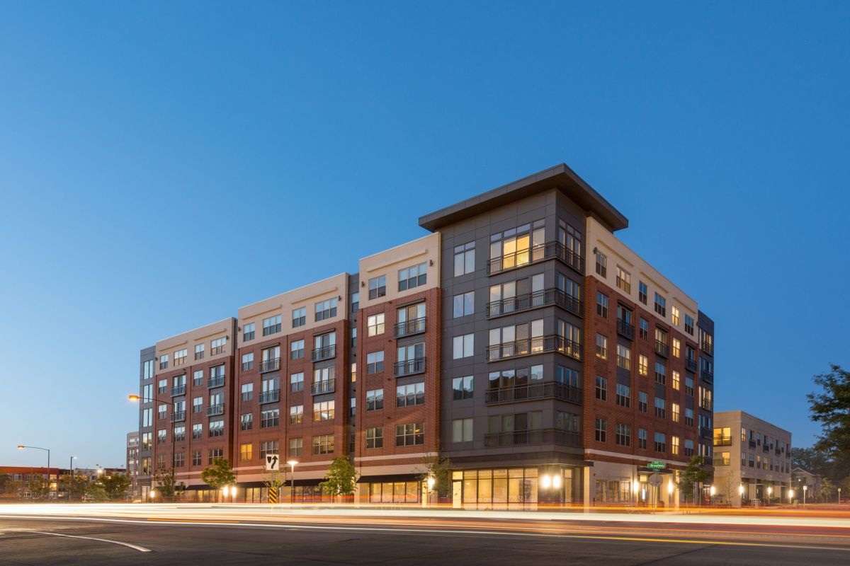 Modern mid-rise apartment building at dusk with lights on and a clear blue sky in the background.