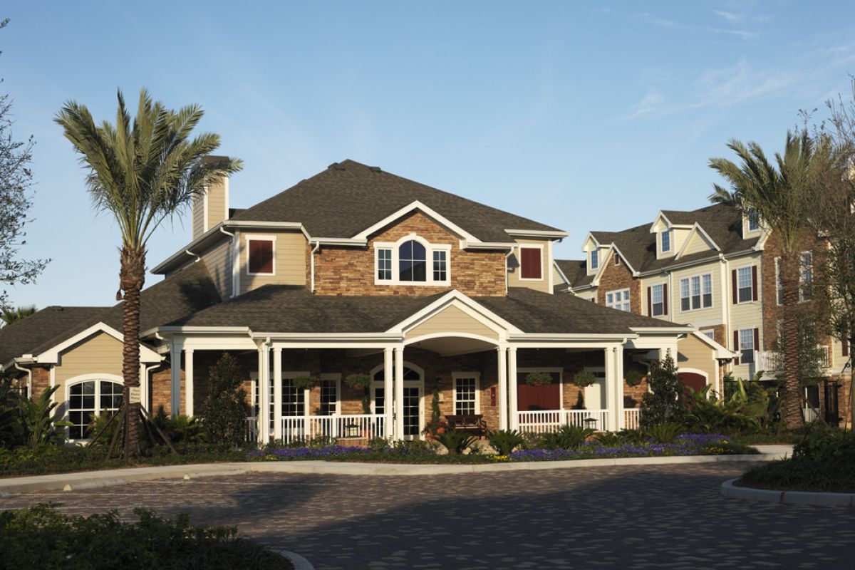 Large two-story house with palm trees, a wraparound porch, and landscaped front yard under a clear sky.