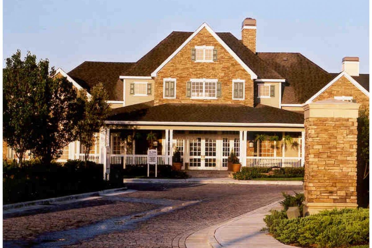 Large two-story house with stone facade, white porch railing, and landscaped front entrance, reminiscent of a Galveston resort.