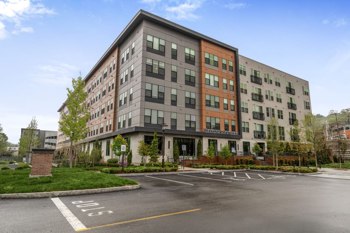 Modern five-story Hanover apartment building with large windows and a mostly empty parking lot in front, located in Stoneham.