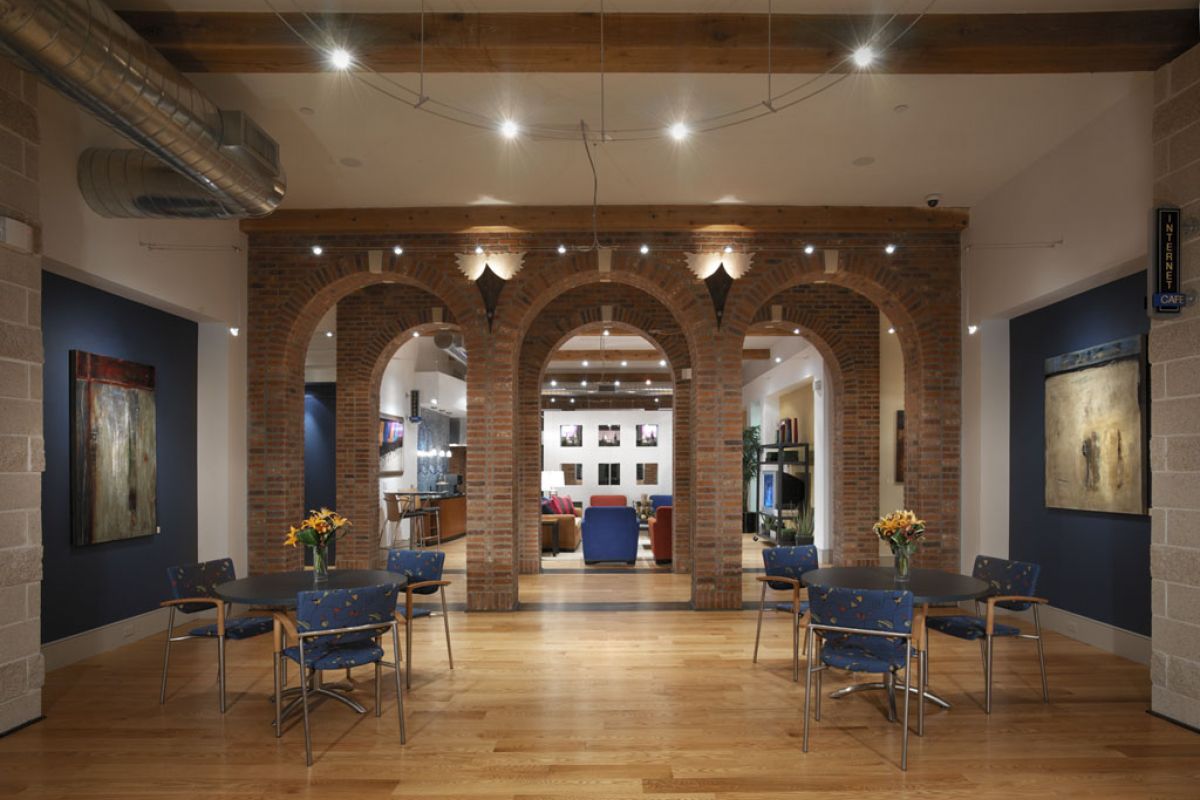 Open lounge area at Hanover West Gray with brick arches, round tables, chairs, wood flooring, and artwork on navy blue walls.