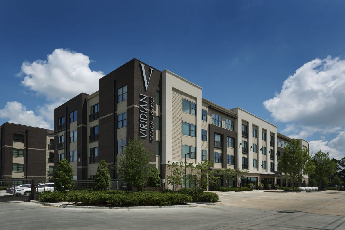 Modern four-story apartment building with "Viridian Design District" sign, blue sky, and landscaped grounds.