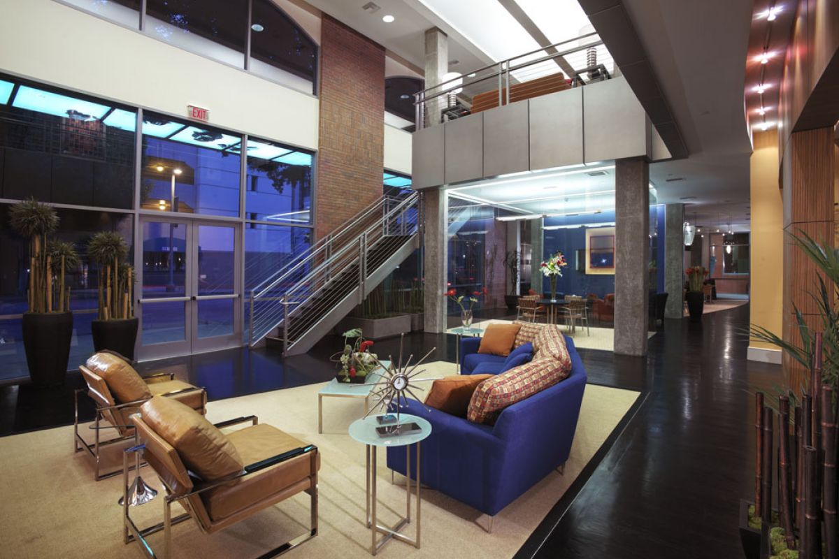 Modern lobby with blue sofa, tan chairs, glass tables, large windows, and indoor plants.