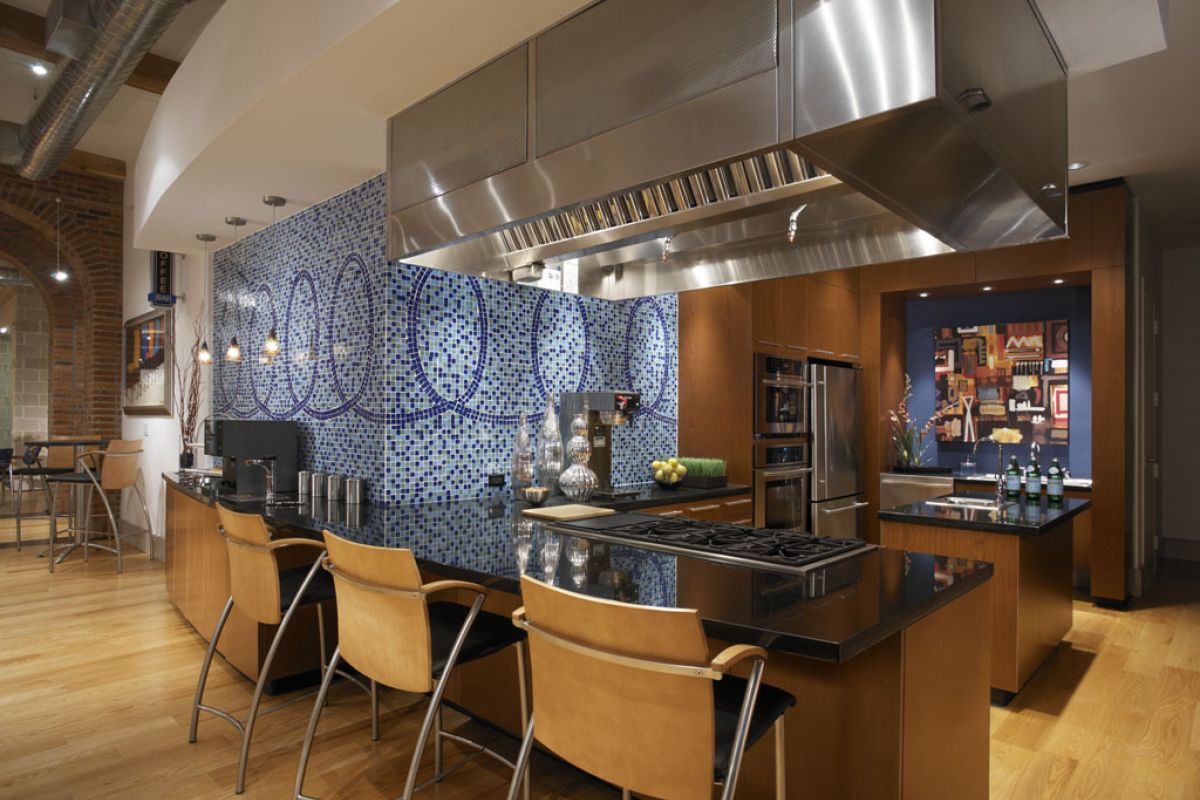 Modern kitchen with blue mosaic backsplash, wood cabinetry, black countertops, and tan bar stools.