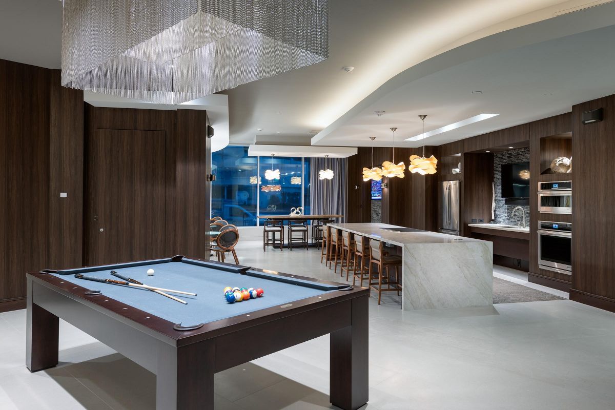 Modern lounge with a pool table, bar seating, kitchen area, and unique pendant lighting.