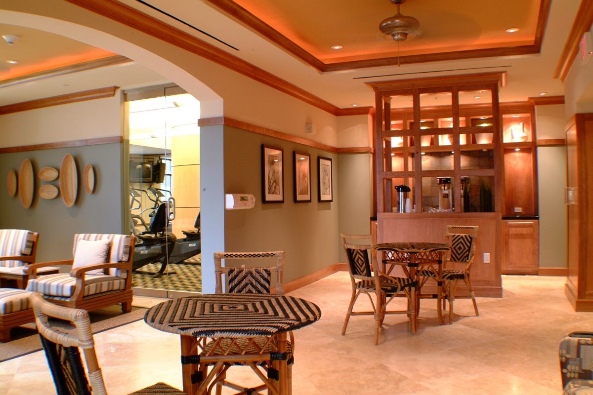 Stylish lounge with wooden furniture, a small bar area, and a window view into a fitness room.