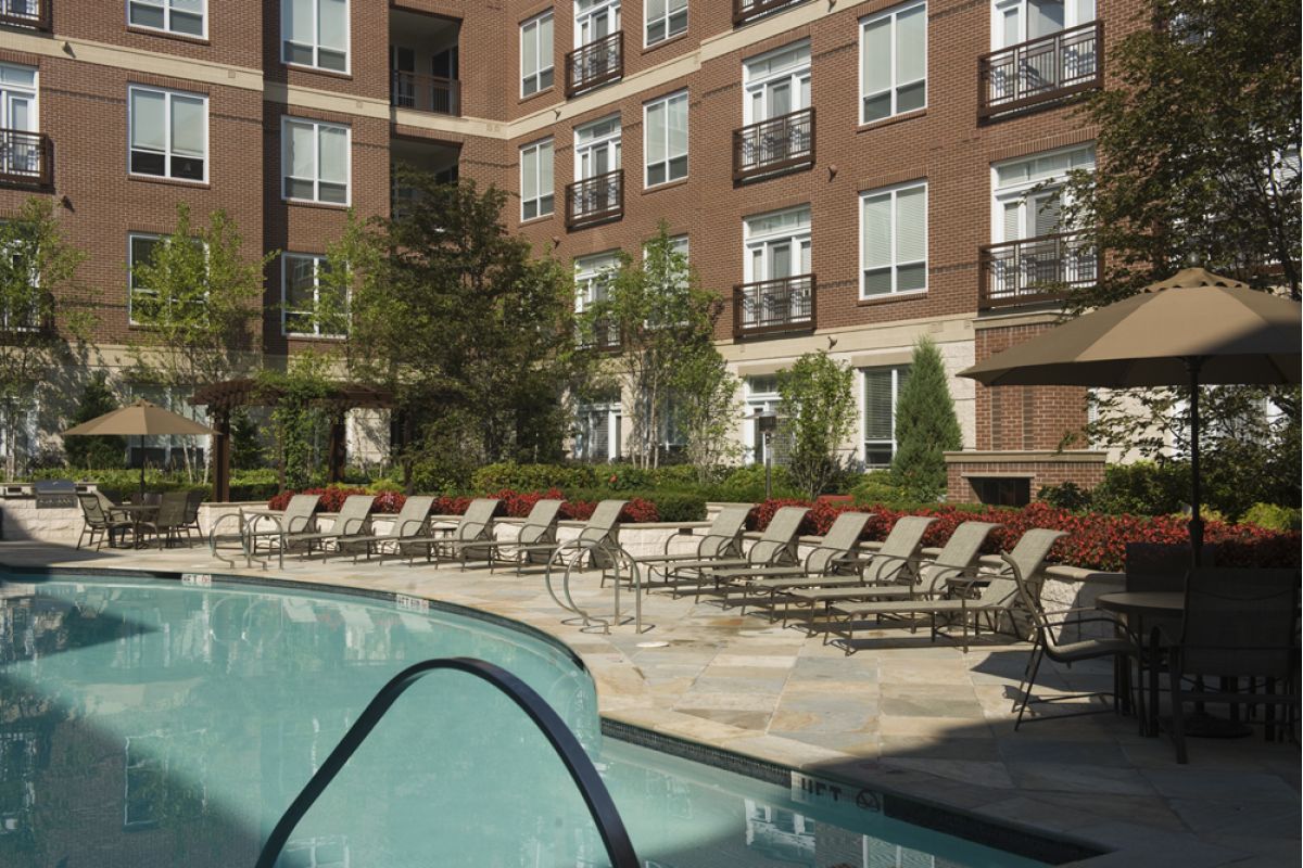 Lounge chairs and umbrellas surround a pool in the Charles River Landing courtyard, offering relaxation at Newton apartments.