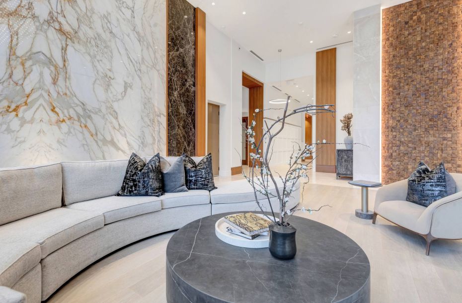 Hanover Company, Hanover Autry Park Elegant modern living room with marble walls, gray sectional sofa, and round coffee table topped with a vase and book.