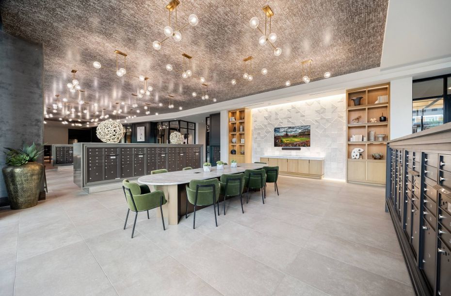 Hanover Company, Hanover RiNo Modern open space with mailboxes, a large table with green chairs, a TV, and decorative lighting.